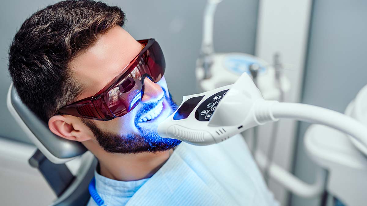 Man undergoing professional teeth whitening with LED light and protective glasses